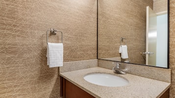 Une salle de bain avec un lavabo doté d’un plan de travail en granit, un grand miroir et un porte-serviettes.