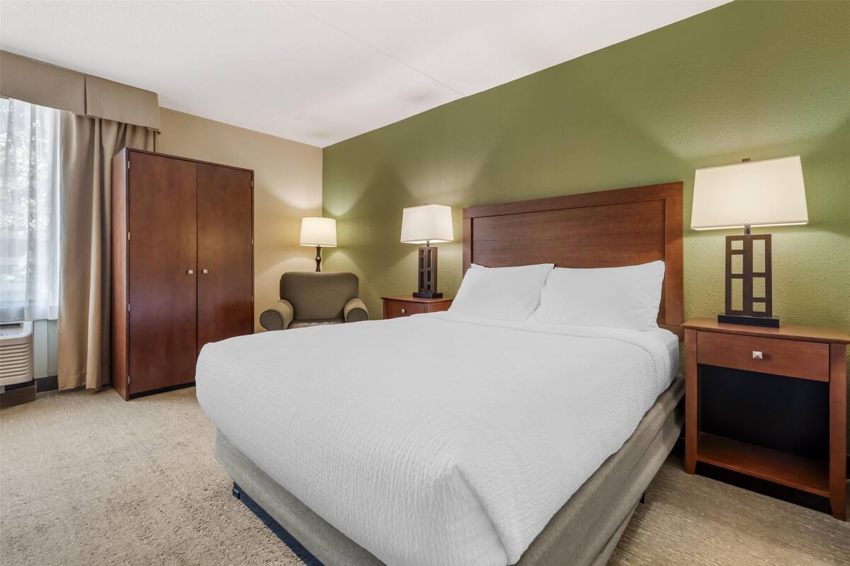 A hotel room with a large bed, two bedside tables with lamps, a wooden wardrobe, and a chair.