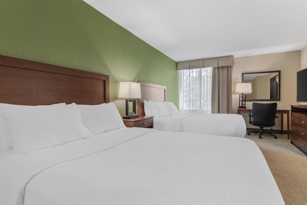 A hotel room with two beds, a desk, a chair, a lamp, and a mirror.