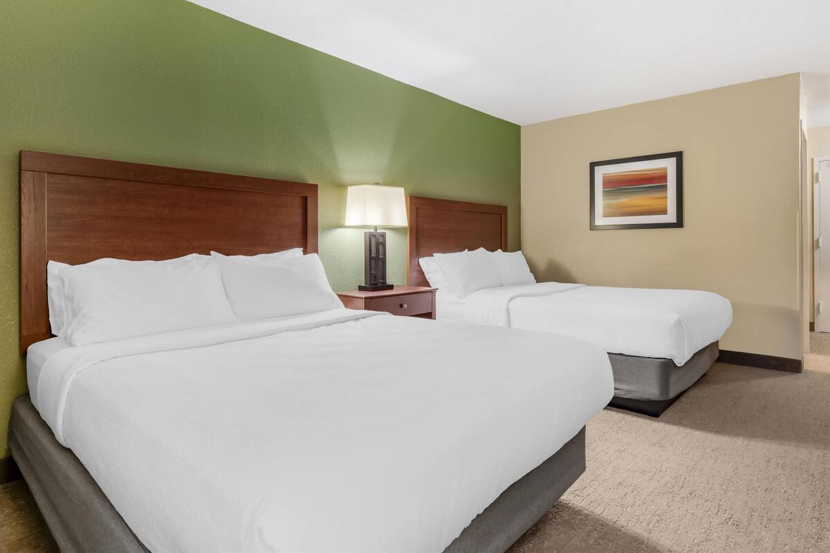 A hotel room with two beds, a nightstand with a lamp, and a painting on the wall.