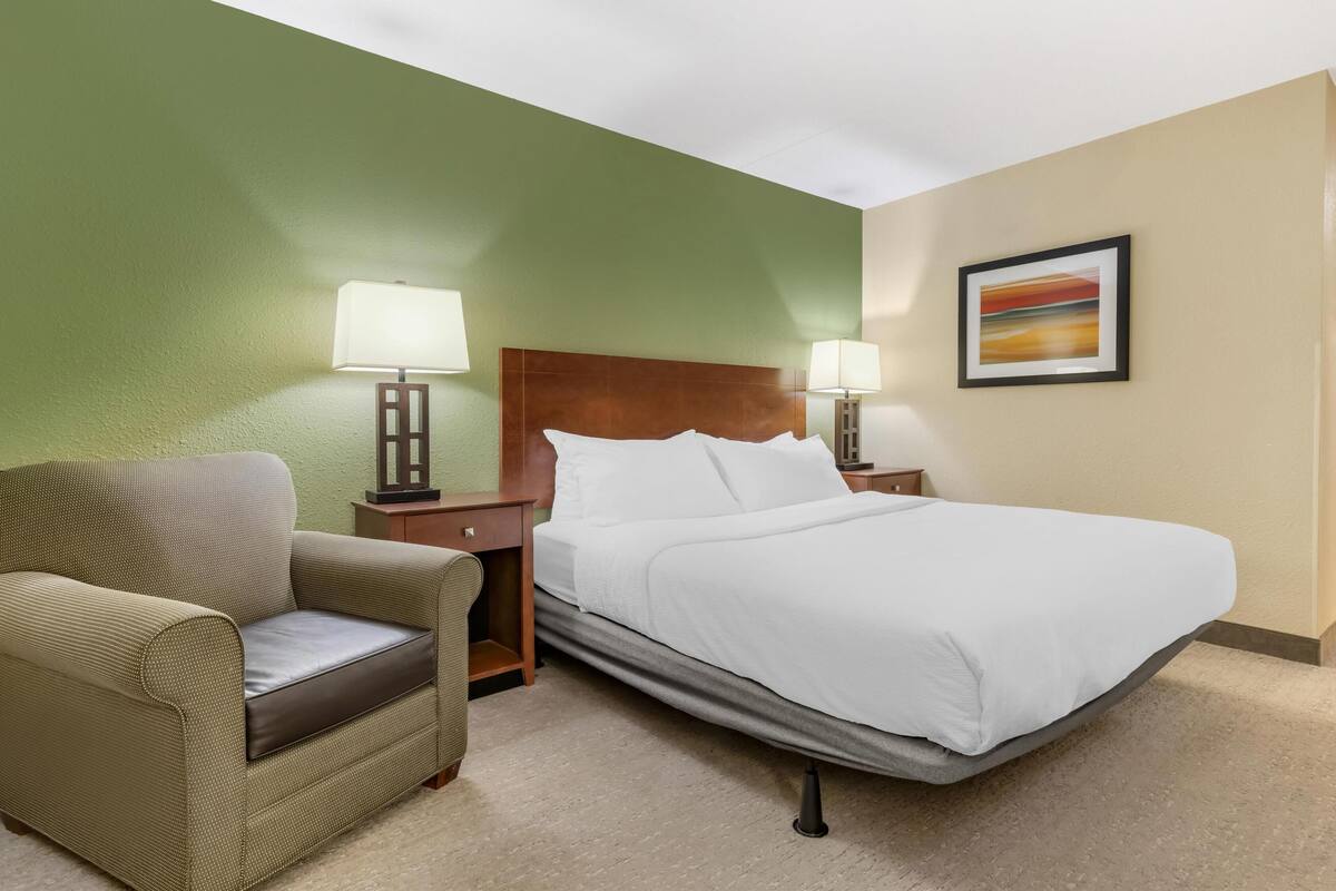 A hotel room with a bed, a chair, two bedside tables with lamps, and a framed picture on the wall.
