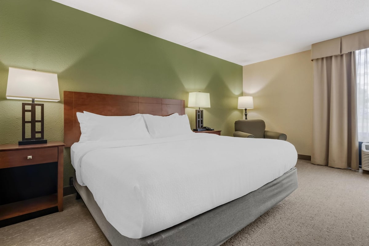 A hotel room with a large bed, two bedside tables with lamps, a chair, and a window with curtains.