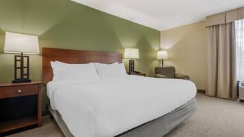 Een hotelkamer met een groot bed, twee nachtkastjes met lampen, een stoel en een raam met gordijnen.