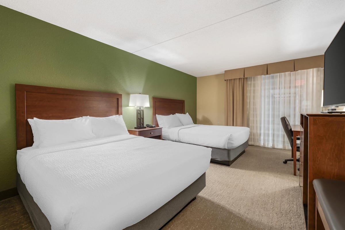 A hotel room with two beds, a desk, and a television.