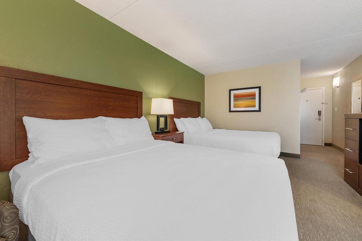 A hotel room with two beds, a nightstand with a lamp, a framed picture on the wall, and a dresser.