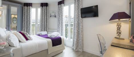 Una habitación de hotel con cama, televisión, escritorio y balcón con cortinas.