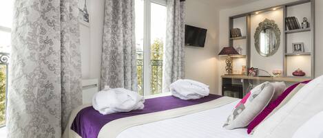 Een hotelkamer met een bed, een bureau, een spiegel en uitzicht op de Eiffeltoren.