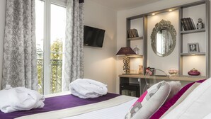 Una habitación de hotel con cama, escritorio, televisión y balcón con cortinas.