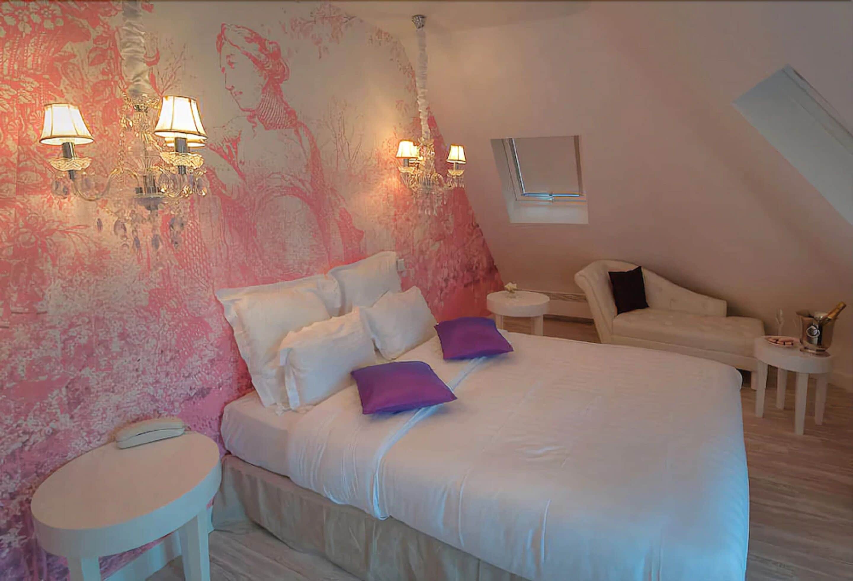 Un dormitorio con una cama grande, dos lámparas de noche, una mesita redonda, una silla y un adornado en la pared.