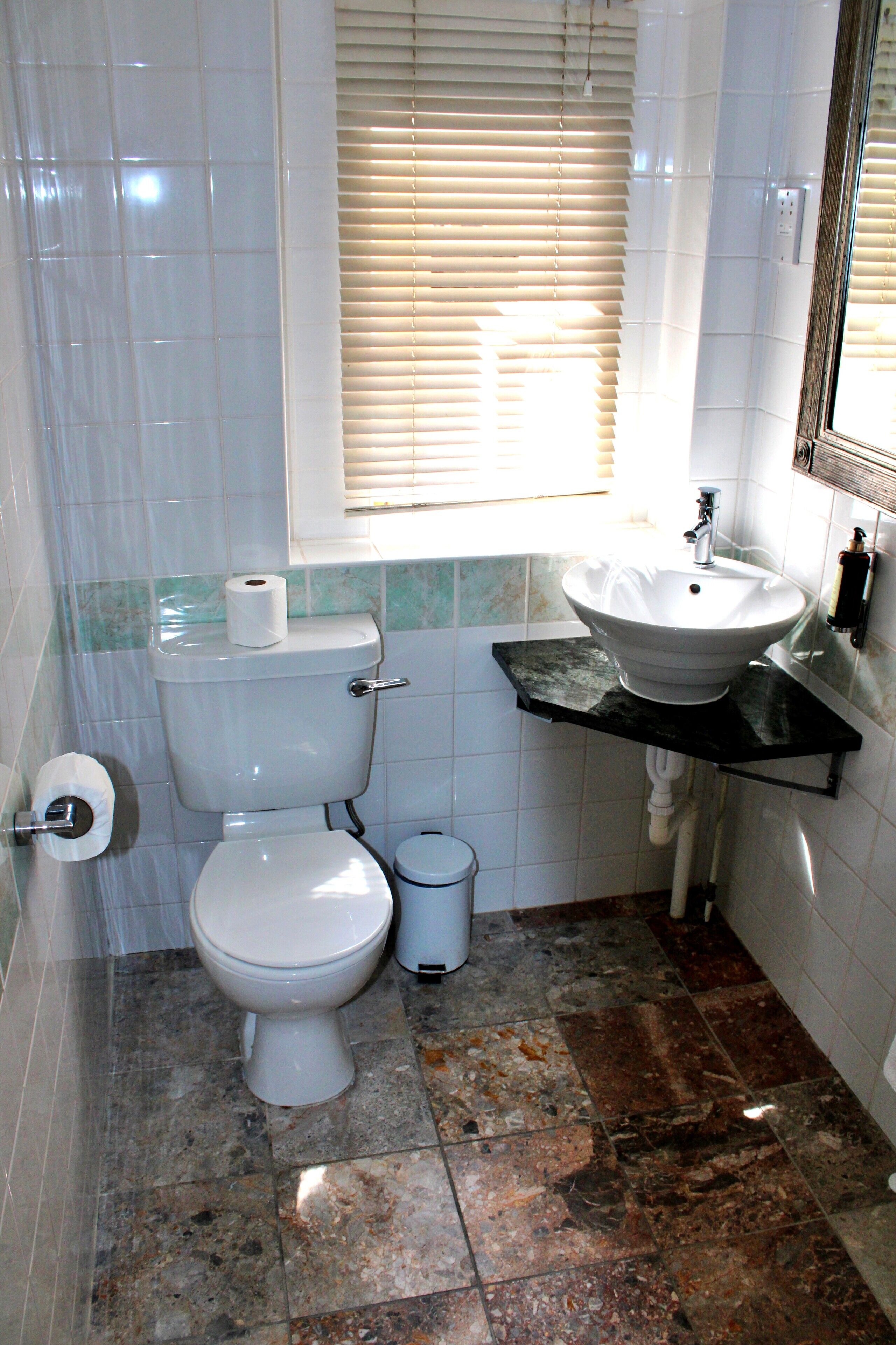 A bathroom with a toilet, sink, and window with blinds.