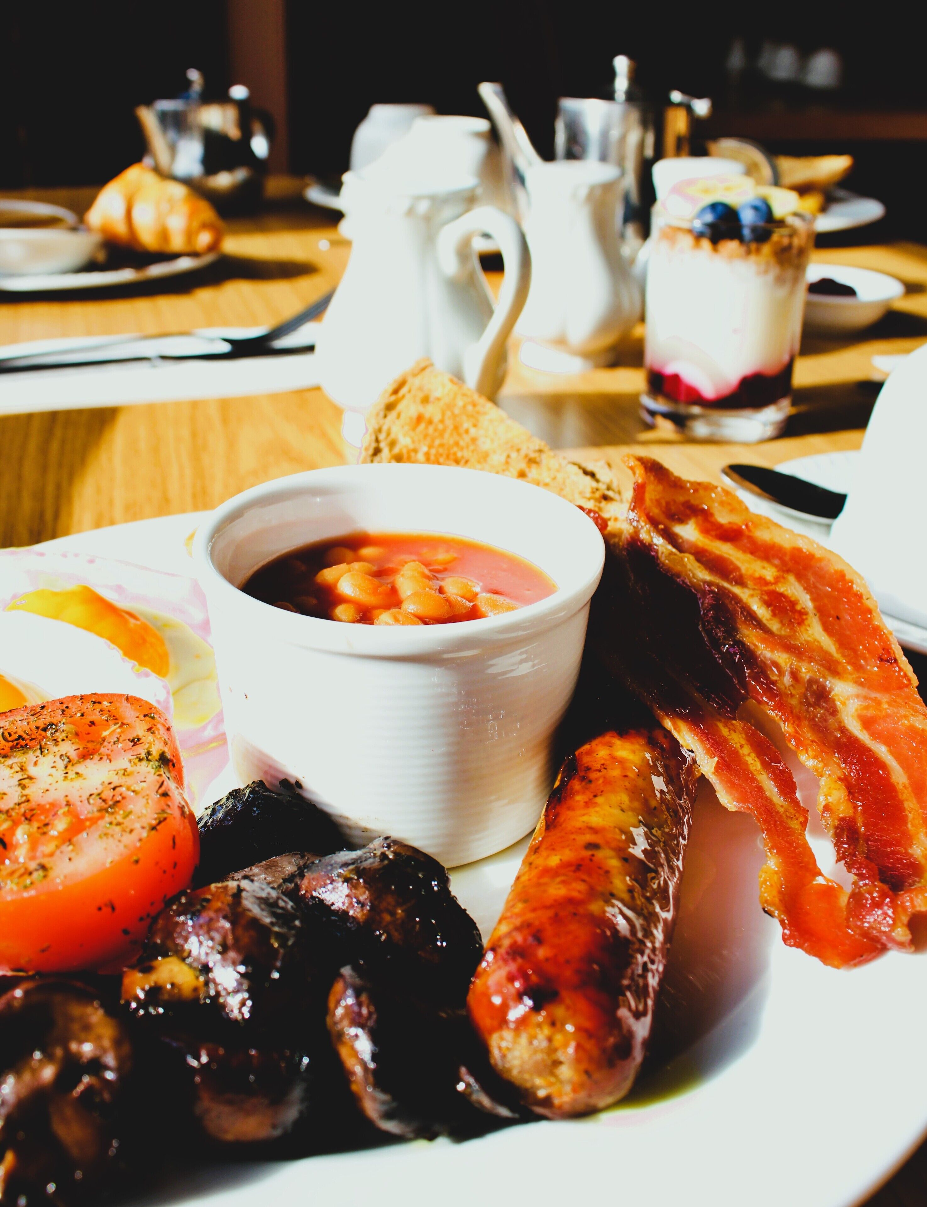 Un plato de desayuno con salchichas, tocino, tomates y frijoles.