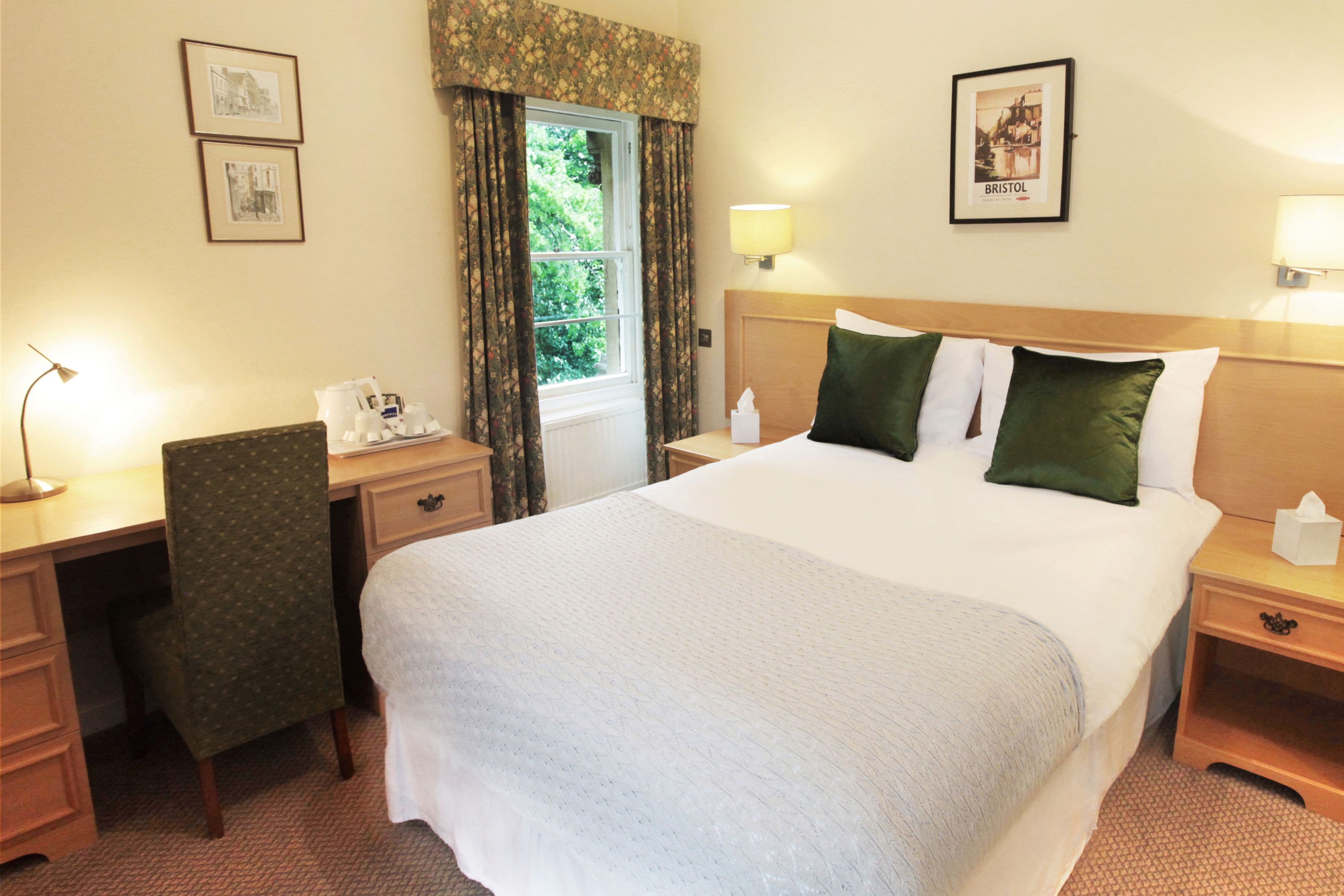 A hotel room with a large bed, a desk with a telephone, a chair, and two bedside tables with lamps.