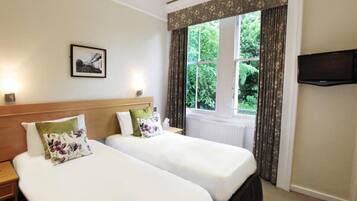 A hotel room with two beds, a television, a window with curtains, and a framed picture on the wall.