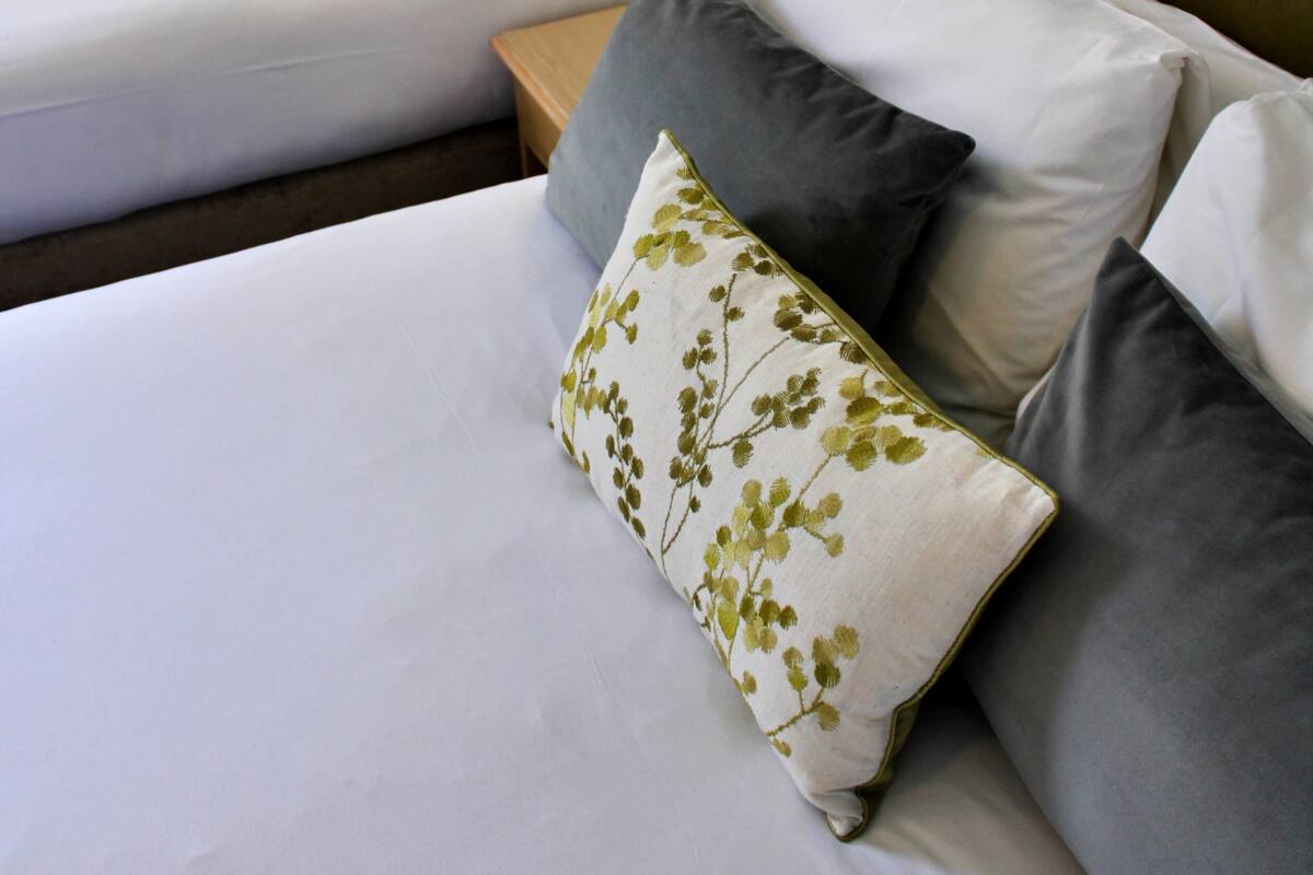 A hotel room with two single beds, each with a wooden headboard and white bedding. There is a nightstand with a lamp between the beds.