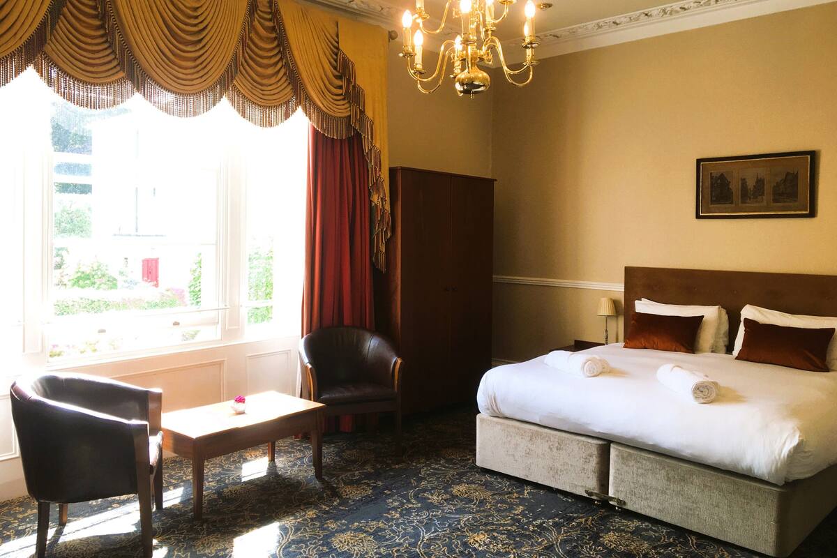 A hotel room with a large bed, a chair, a table, and a chandelier.