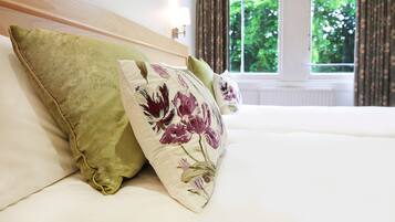A bed with floral pillows and a view of greenery through a window.