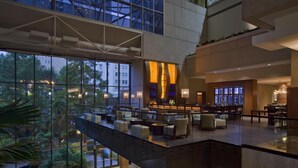 Un moderno vestíbulo de hotel con un atrio de vidrio, zonas de estar y un bar.