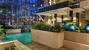 Un área de piscina interior moderna con barandillas de cristal, una fuente de agua y plantas de interior.