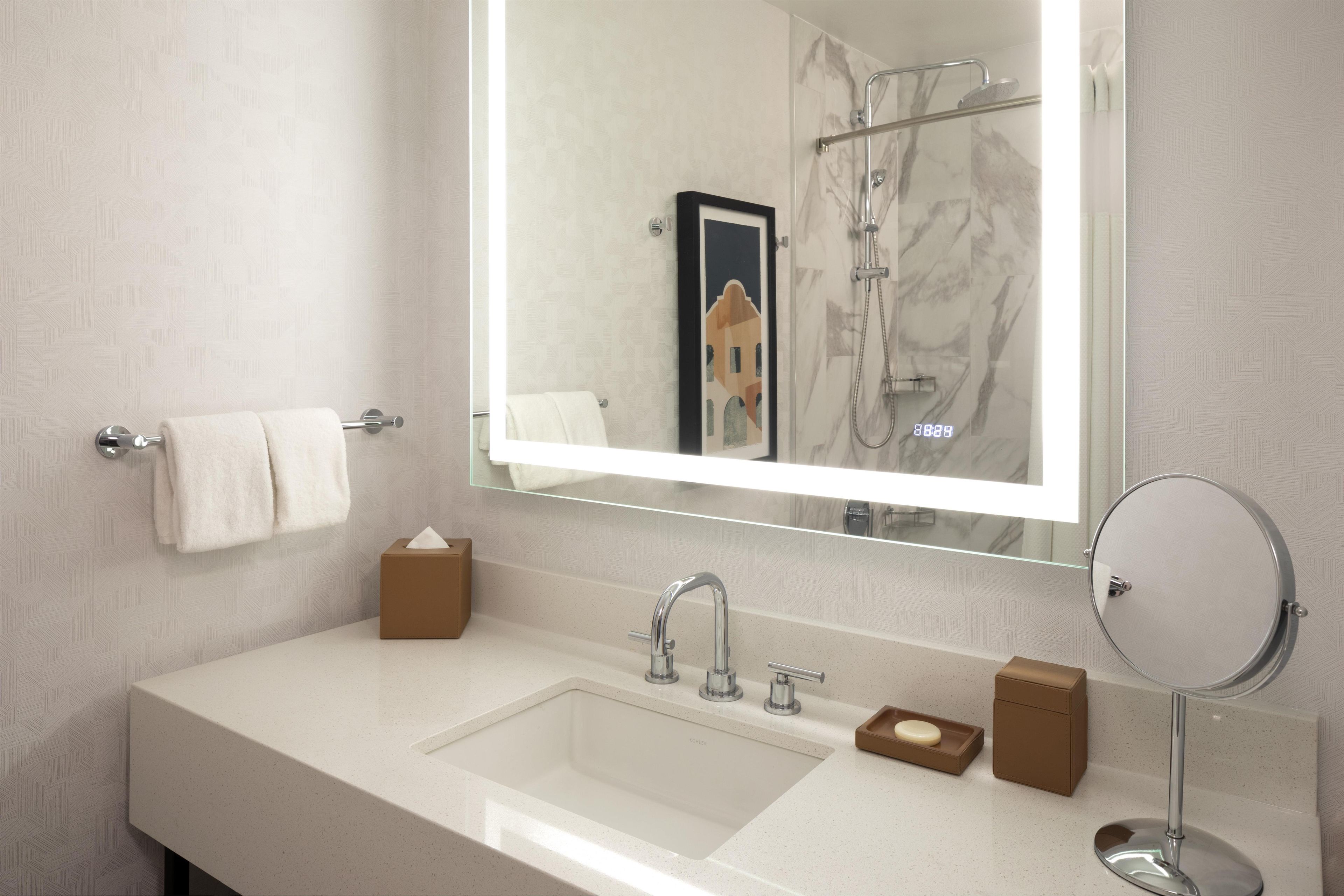 A bathroom with a large mirror, a sink, a towel rack, and a shower.