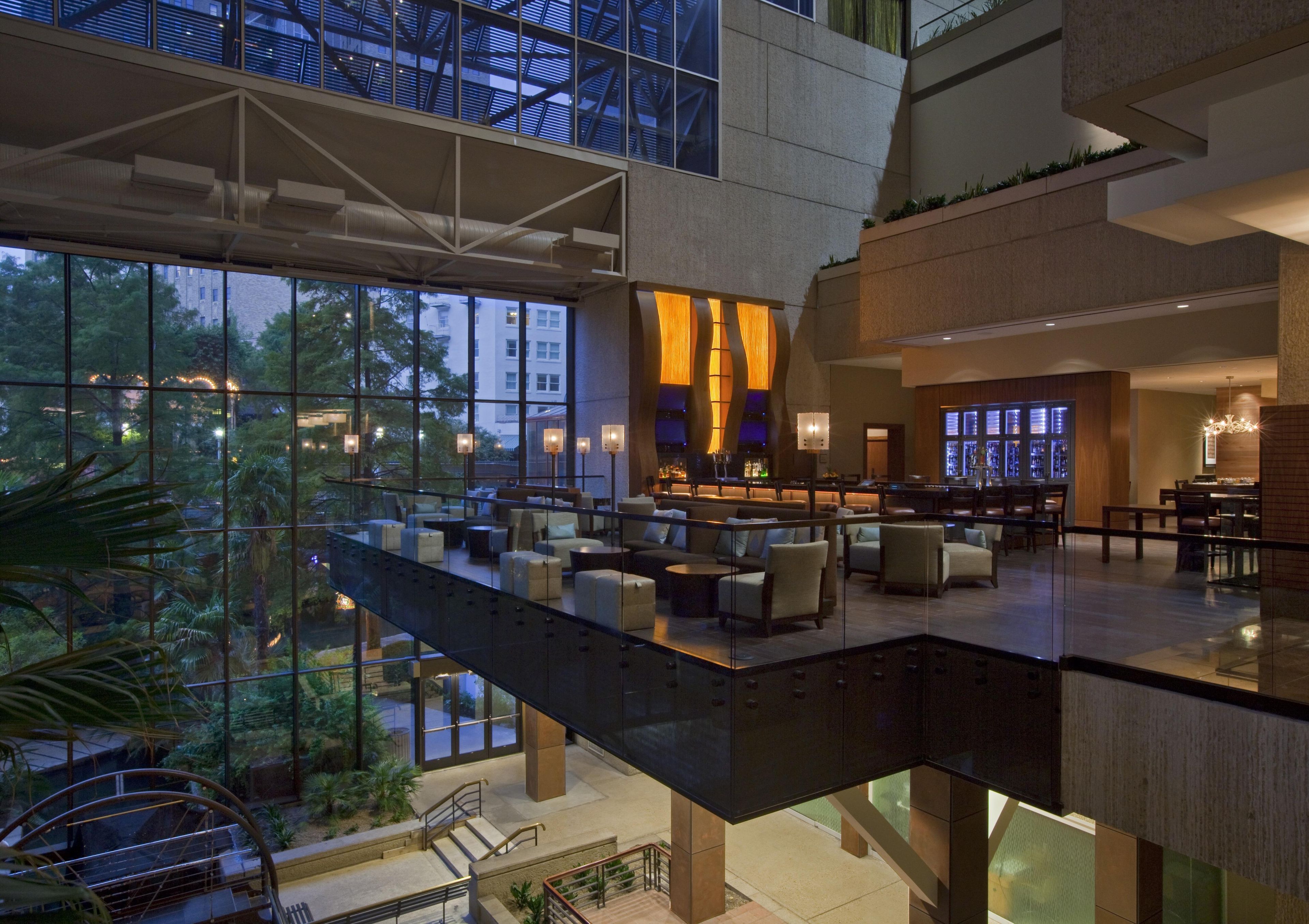 A modern hotel lobby with a glass atrium, seating areas, and a bar.