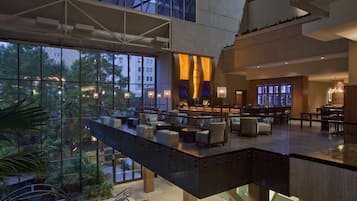 A modern hotel lobby with a glass atrium, seating areas, and a bar.