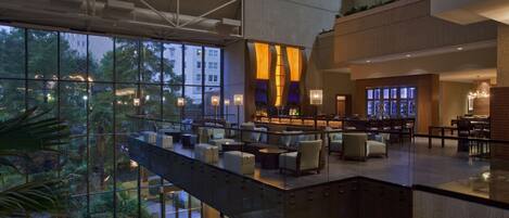A modern hotel lobby with a glass atrium, seating areas, and a bar.