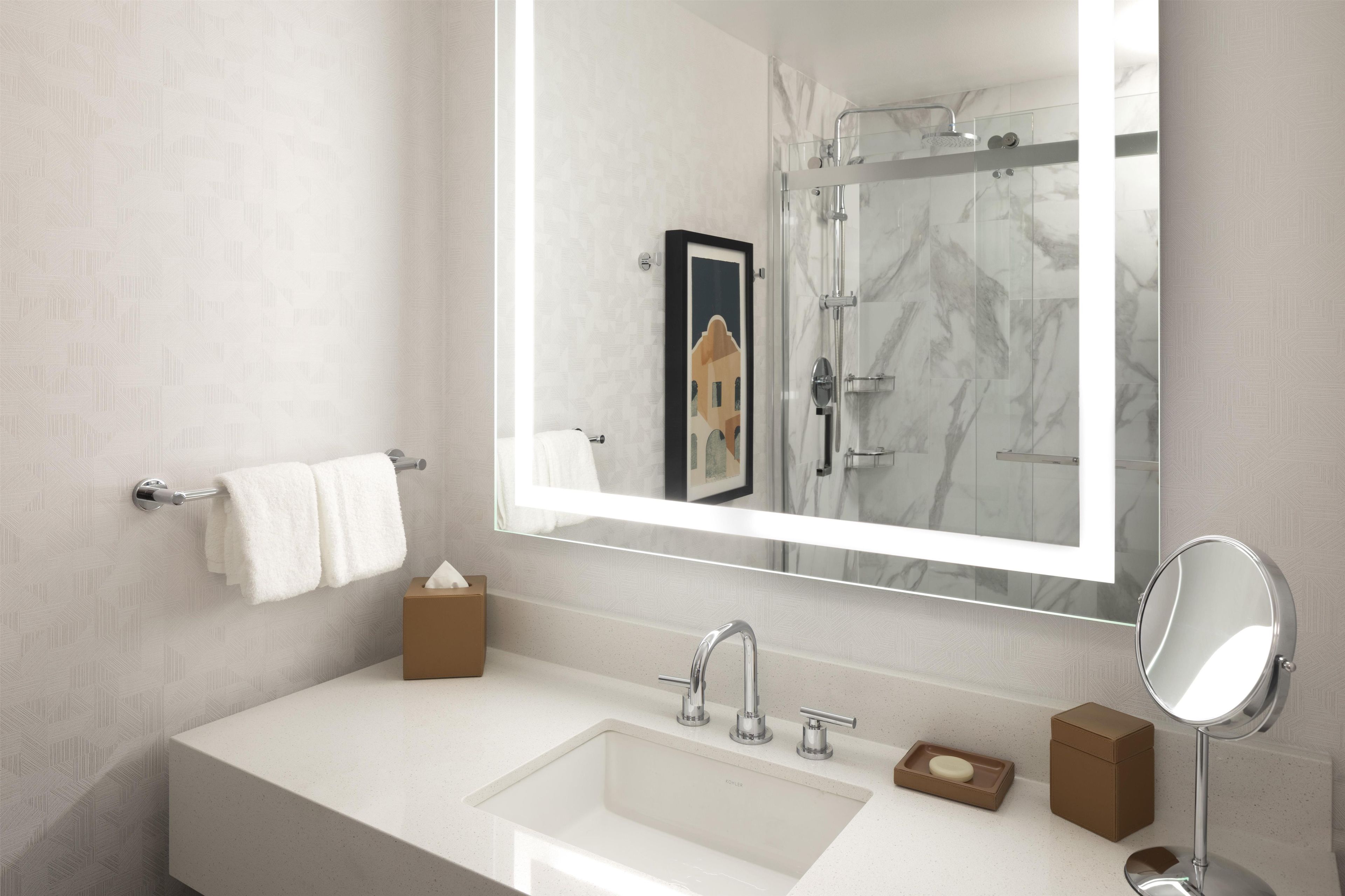 A modern bathroom with a large mirror, a sink, and a shower.