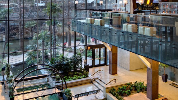 Un área de piscina interior moderna con barandales de vidrio, asientos y una zona de bar con pantallas.