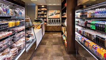 Una zona de comidas bien iluminada con diversas opciones de alimentos y bebidas, que incluye una barra de delicatessen y dispensadores de bebidas.