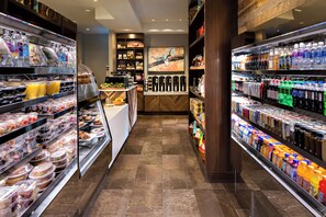 Un espace de restauration bien éclairé, offrant une variété de choix de plats et de boissons, notamment un comptoir de produits de charcuterie et des distributeurs de boissons.