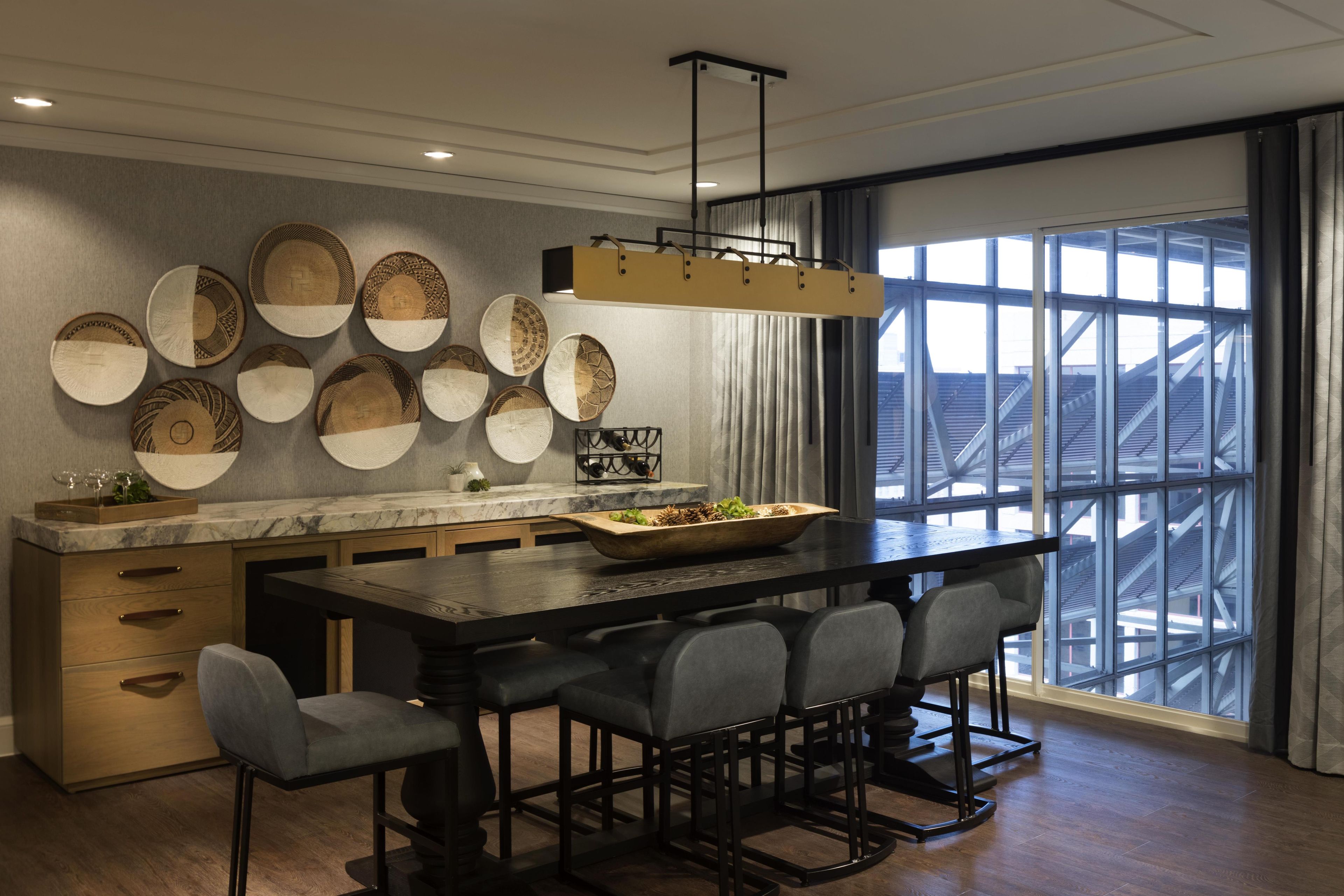 A modern kitchen with a large island, multiple hanging baskets, and a view through large windows.