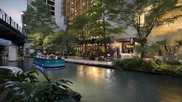 A riverside walkway with a boat ride, surrounded by greenery and modern buildings.