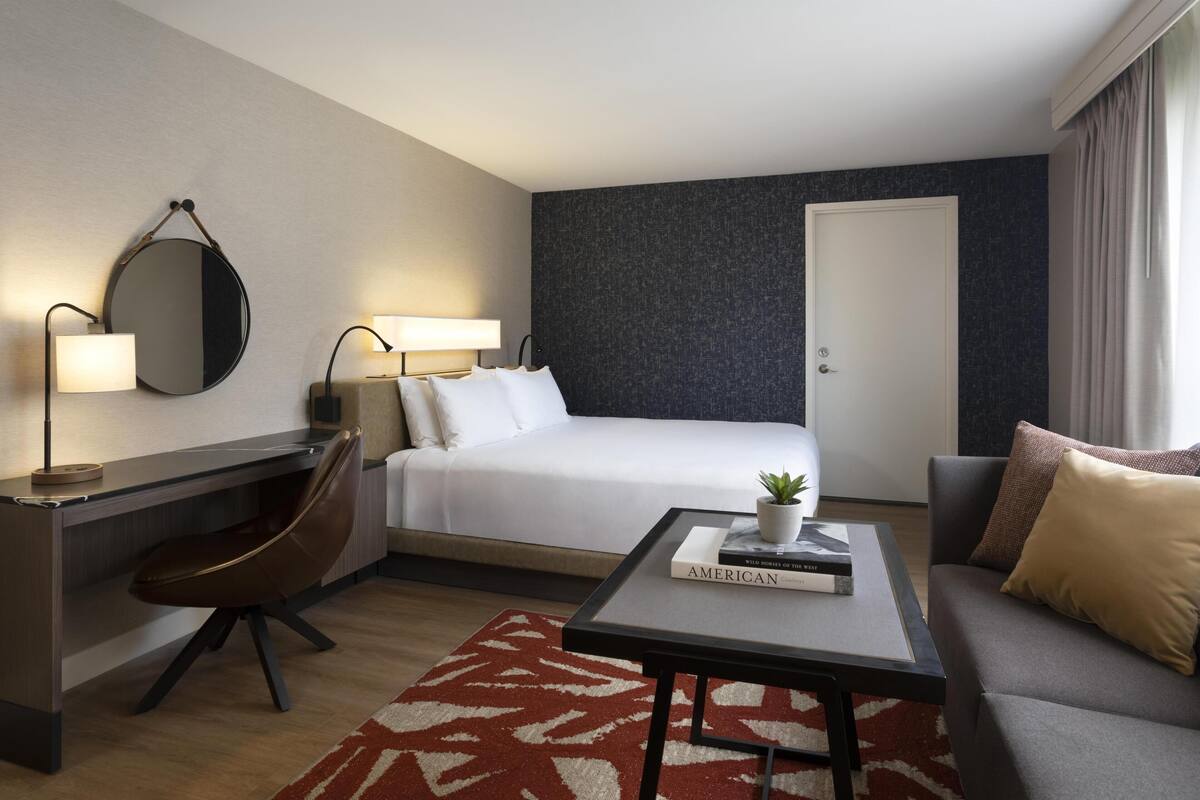 Habitación de hotel con cama, escritorio, silla, mesa de centro y un espejo grande.