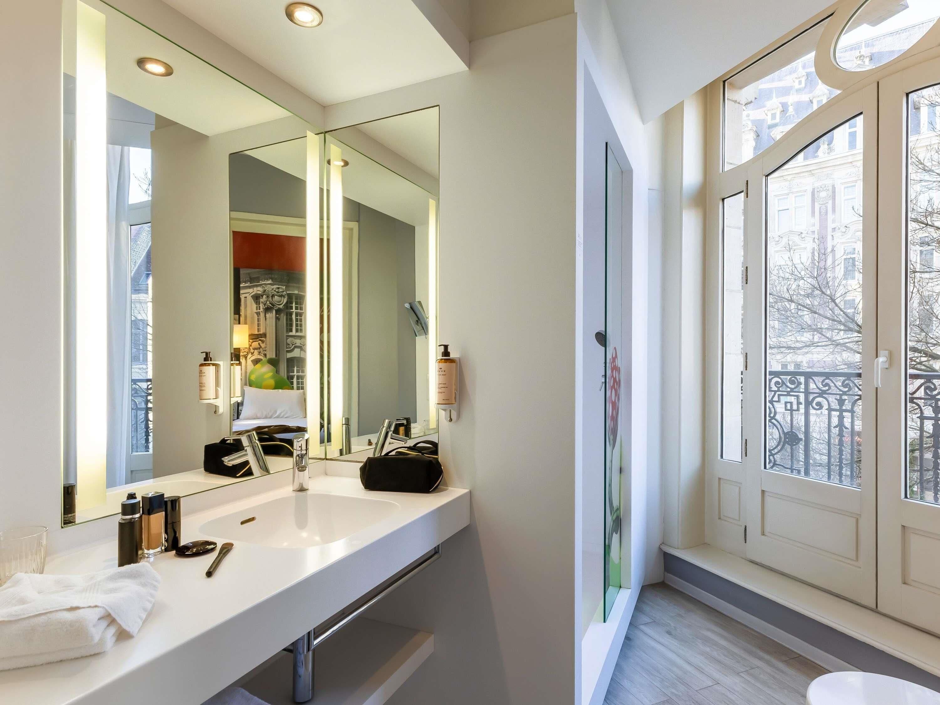 Un baño moderno con un espejo grande, un lavamanos blanco y vistas a la ciudad a través de amplios ventanales.