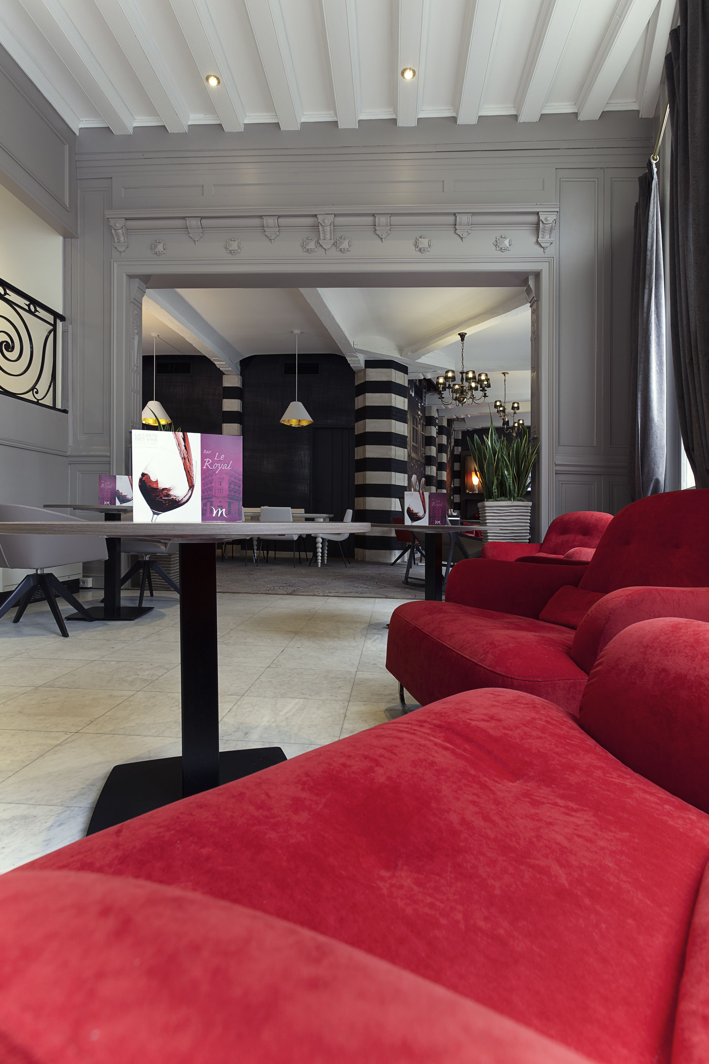 Un salon moderne avec des canapés rouges, un coin repas avec des chaises à rayures et un lustre.