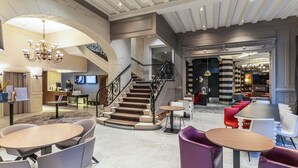 Un amplio vestíbulo con una imponente escalera, zonas de estar modernas y un mostrador de recepción.