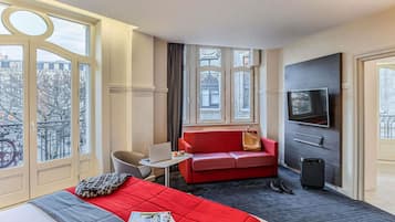 Ein Hotelzimmer mit einem Bett, einem roten Sofa, einem Fernseher und einem Fenster mit Blick auf Gebäude.