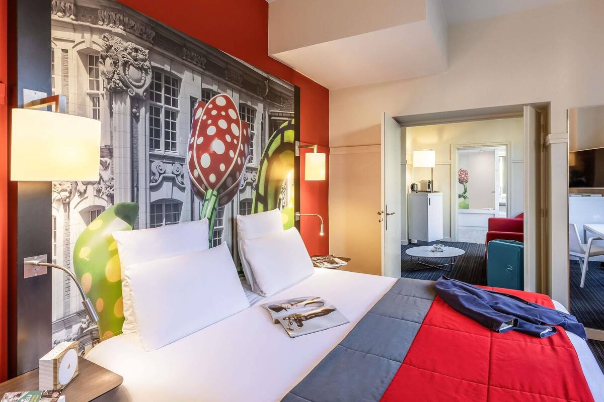 A hotel room with a bed, a desk, a chair, a mirror, and a door leading to a bathroom.