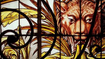 A stained glass window with a lion's face and floral patterns.