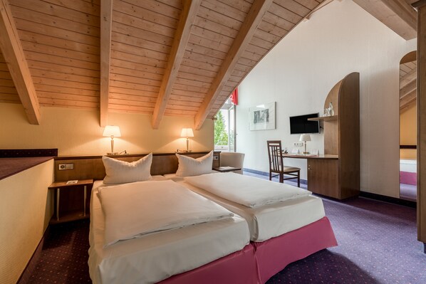 A hotel room with a wooden ceiling, a bed with white bedding, a desk with a chair, and a television on the wall. - Andante Hotel Dresden (Dresden)