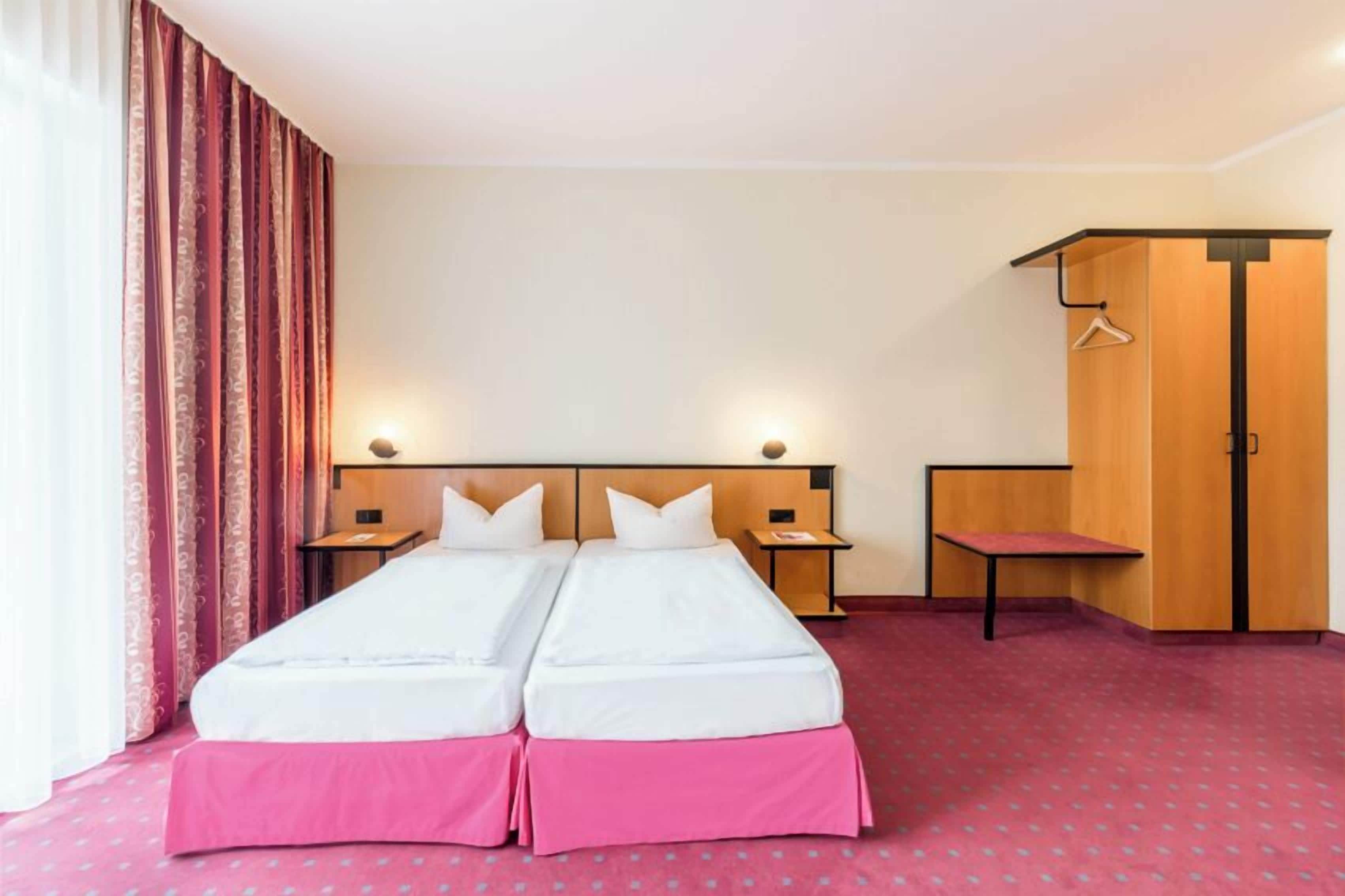 Ein Hotelzimmer mit Doppelbett, Holzschrank, kleinem Tisch und Stuhl.