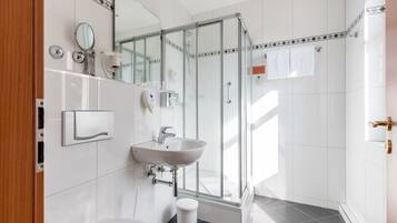 Et moderne badeværelse med en brusekabine i glas, en hvid vask og et toilet.