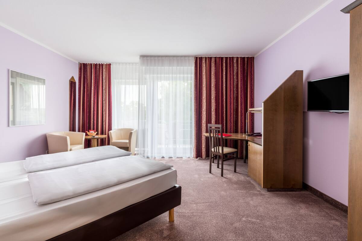 A hotel room with a bed, a desk, a chair, and a television.