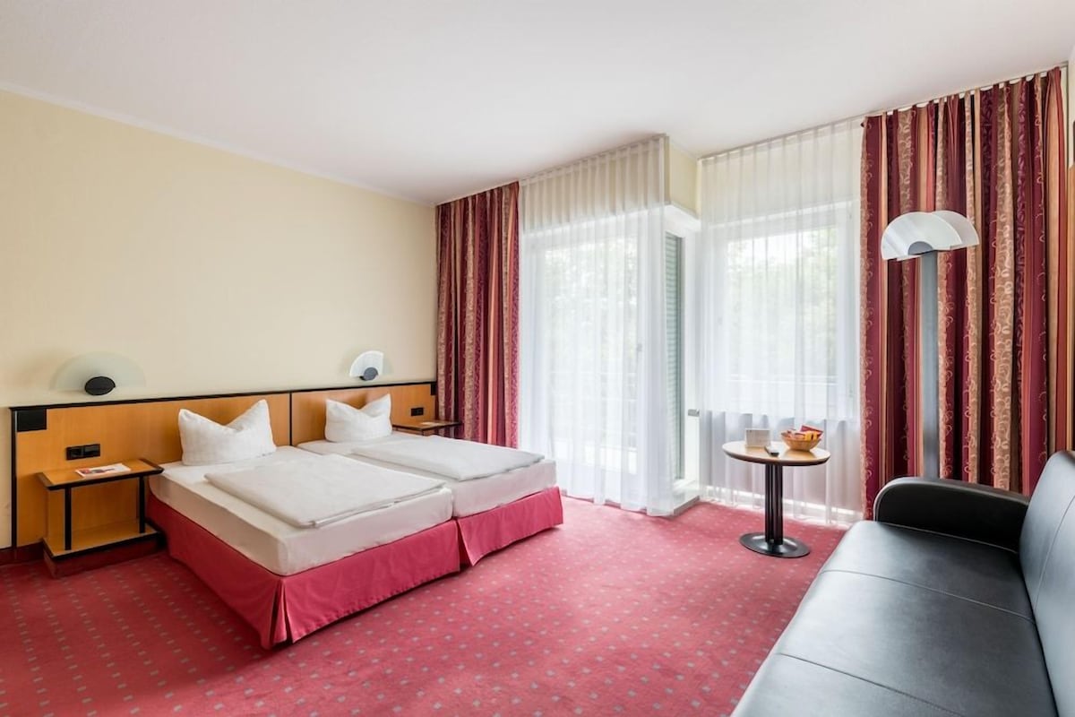 A hotel room with two beds, a sofa, a small table, and a lamp.