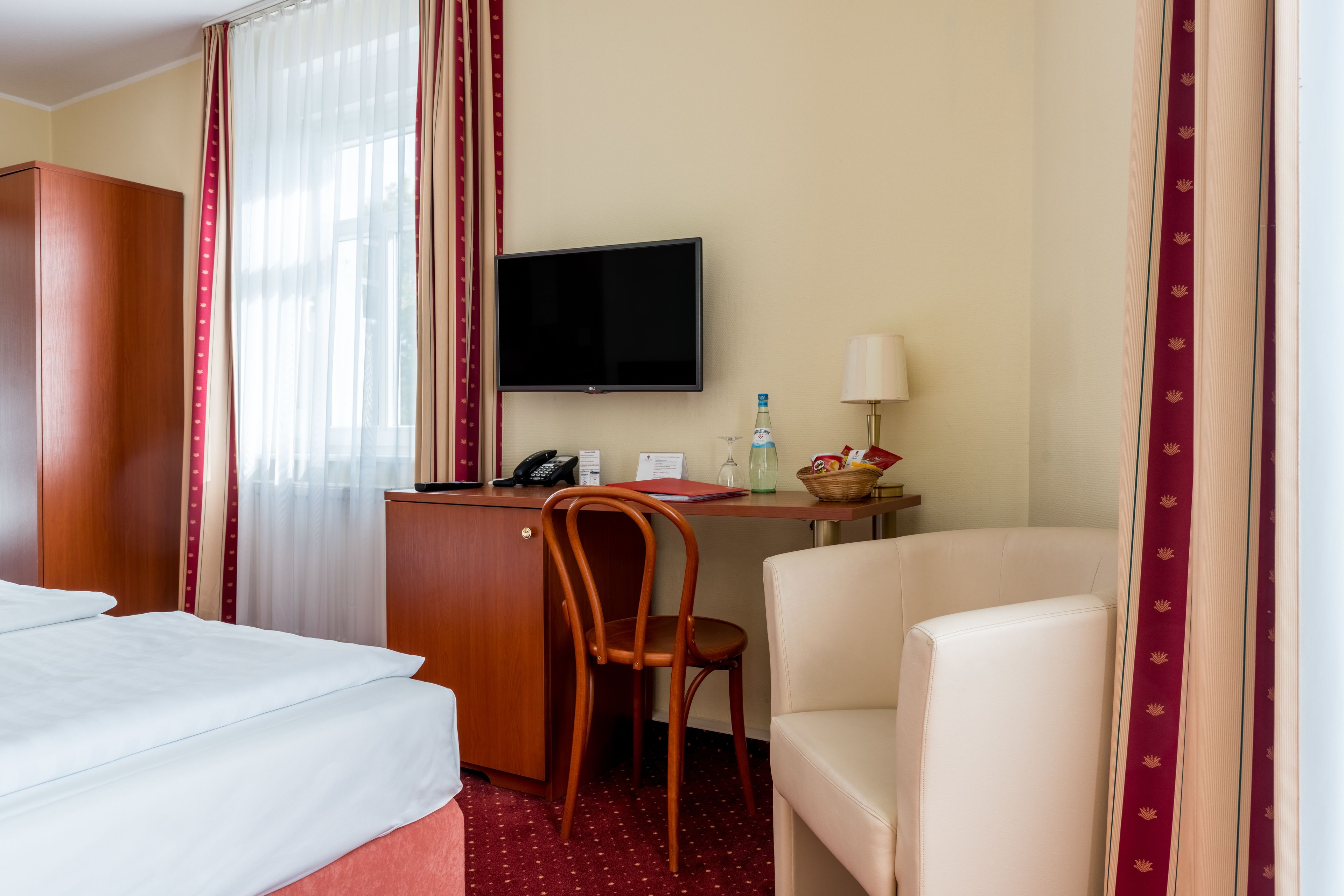 A hotel room with a bed, a desk with a chair, a television, and a lamp.