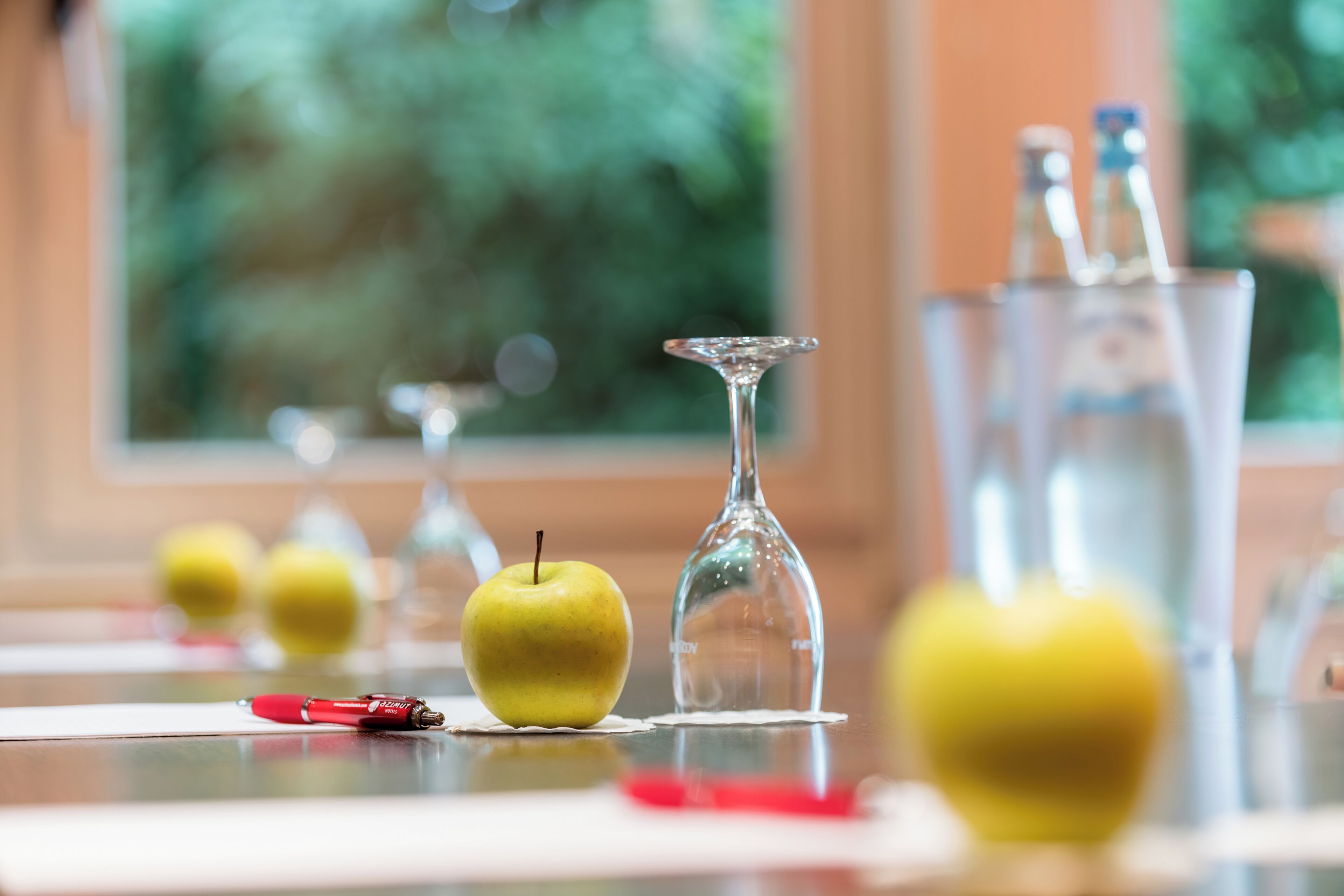 A table with a glass vase, a bottle, and apples.