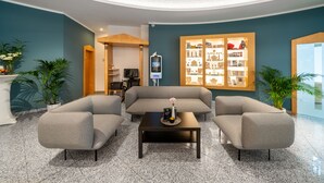 A modern lobby with a grey sofa, two armchairs, a coffee table, and a large bookshelf. - Andante Hotel Dresden (Dresden)