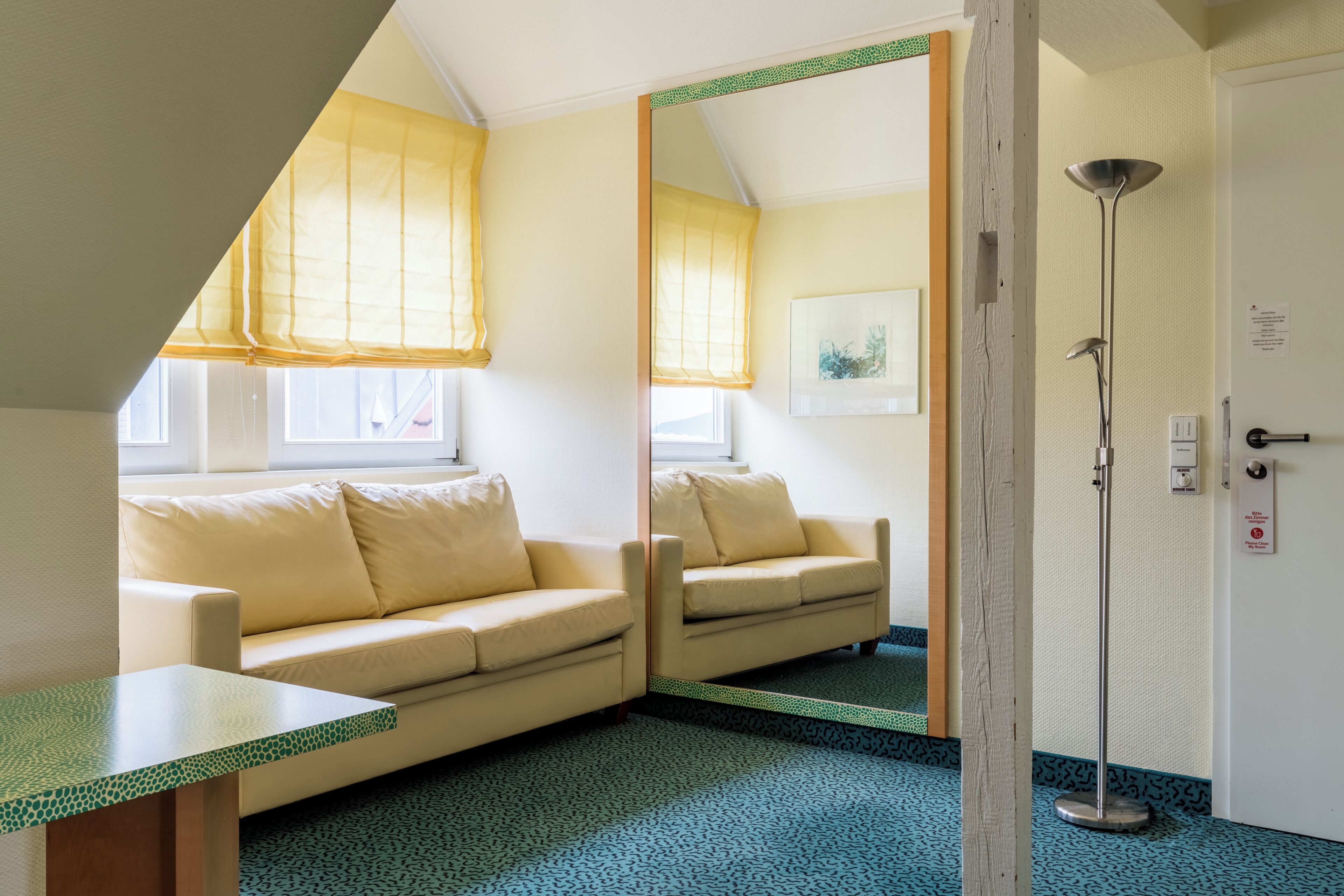 Una habitación con sofá, espejo, lámpara de pie y una puerta con un letrero.