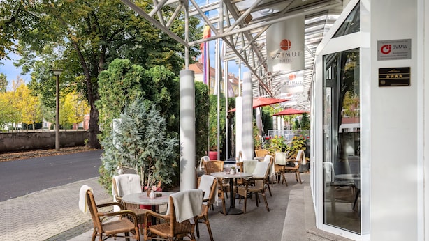 An outdoor seating area with wicker chairs and tables, a covered patio, and a view of the street. - Andante Hotel Dresden (Dresden)