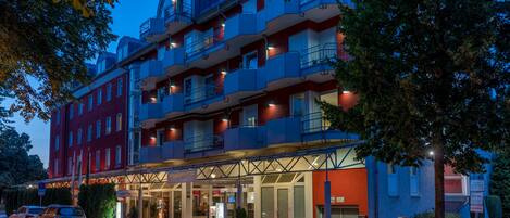 A multi-story hotel with a red facade, balconies, and a covered entrance area.
